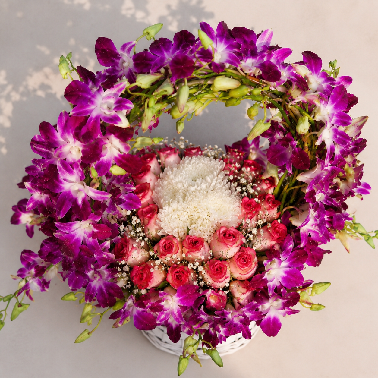 Royal Orchid Bloom Basket featuring fresh purple orchids, pink roses, white carnations, baby's breath and seasonal greenery in a premium white wicker basket.