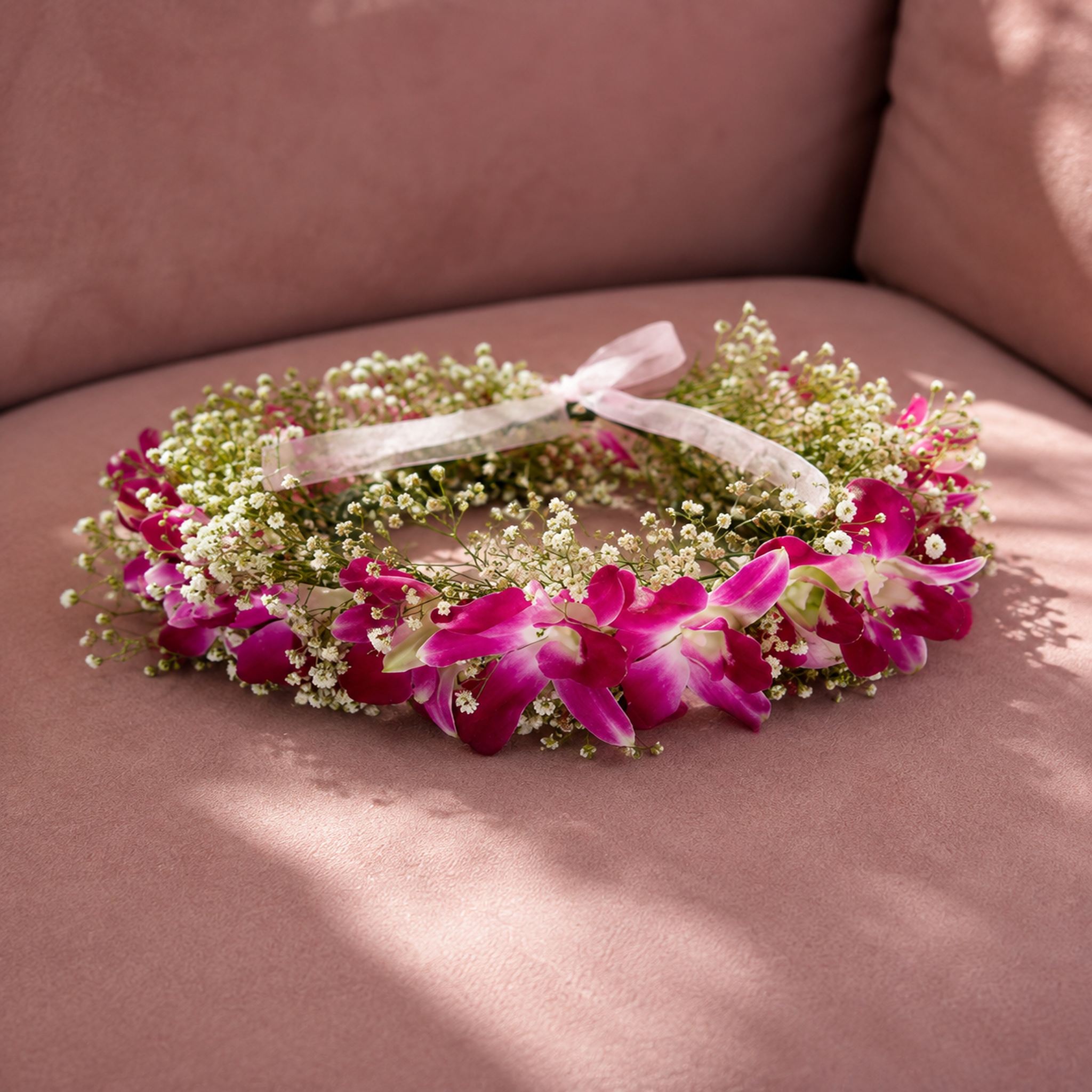 Floral tiara with pink orchids and baby's breath on a pink sofa